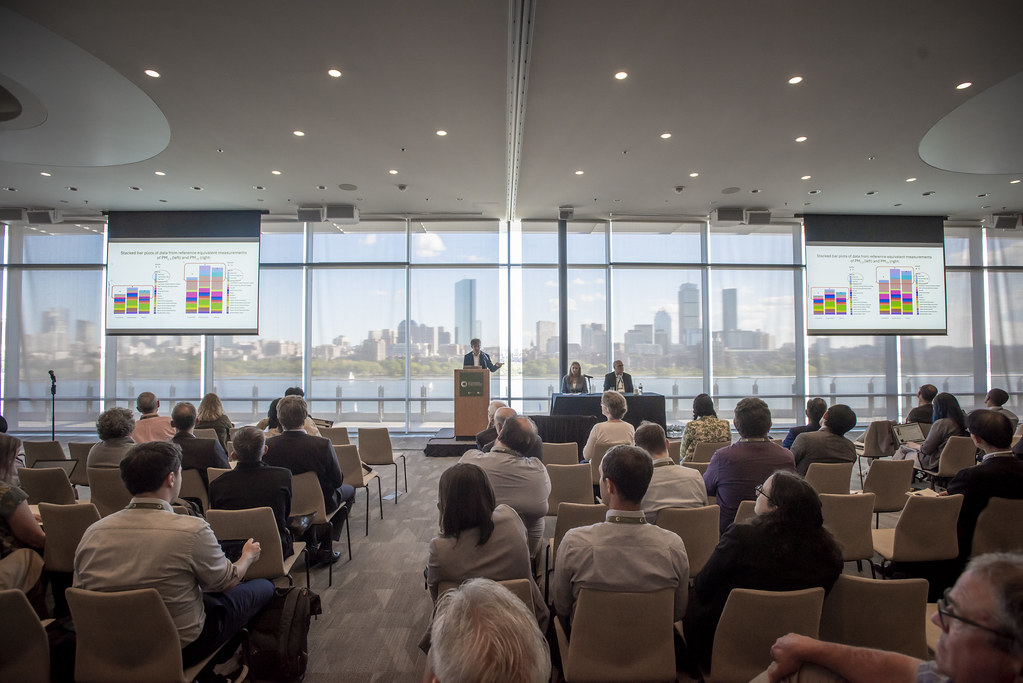 A speaker at the 2025 Tire Emissions Research Conference with Boston skyline in the background