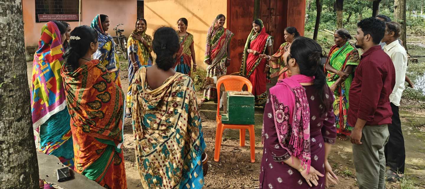 Group of women speaking to each other while standing in a circle around a beehive