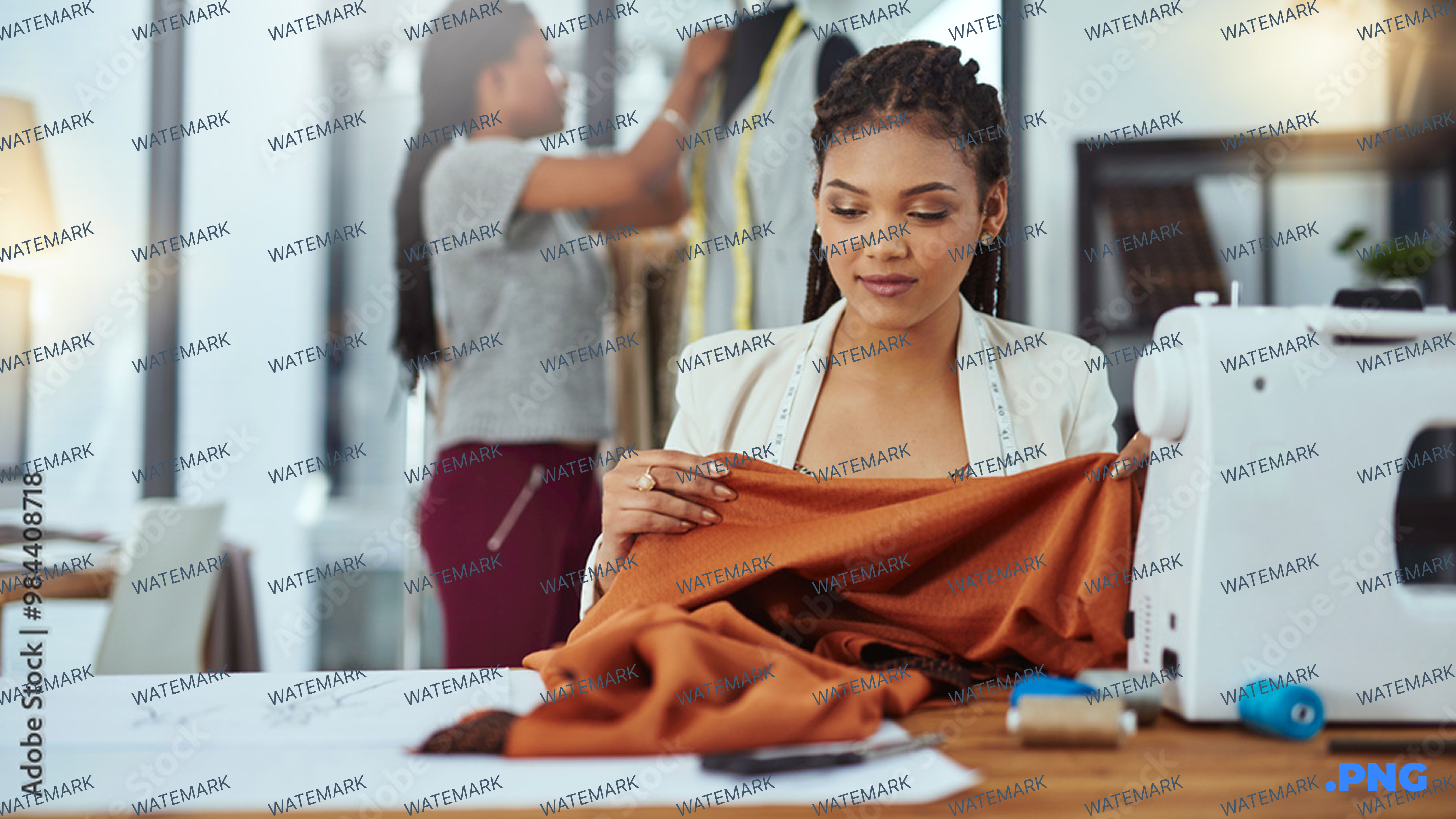 Image of a woman holding orange fabric who appears to be sitting on a table with a sewing machine. 